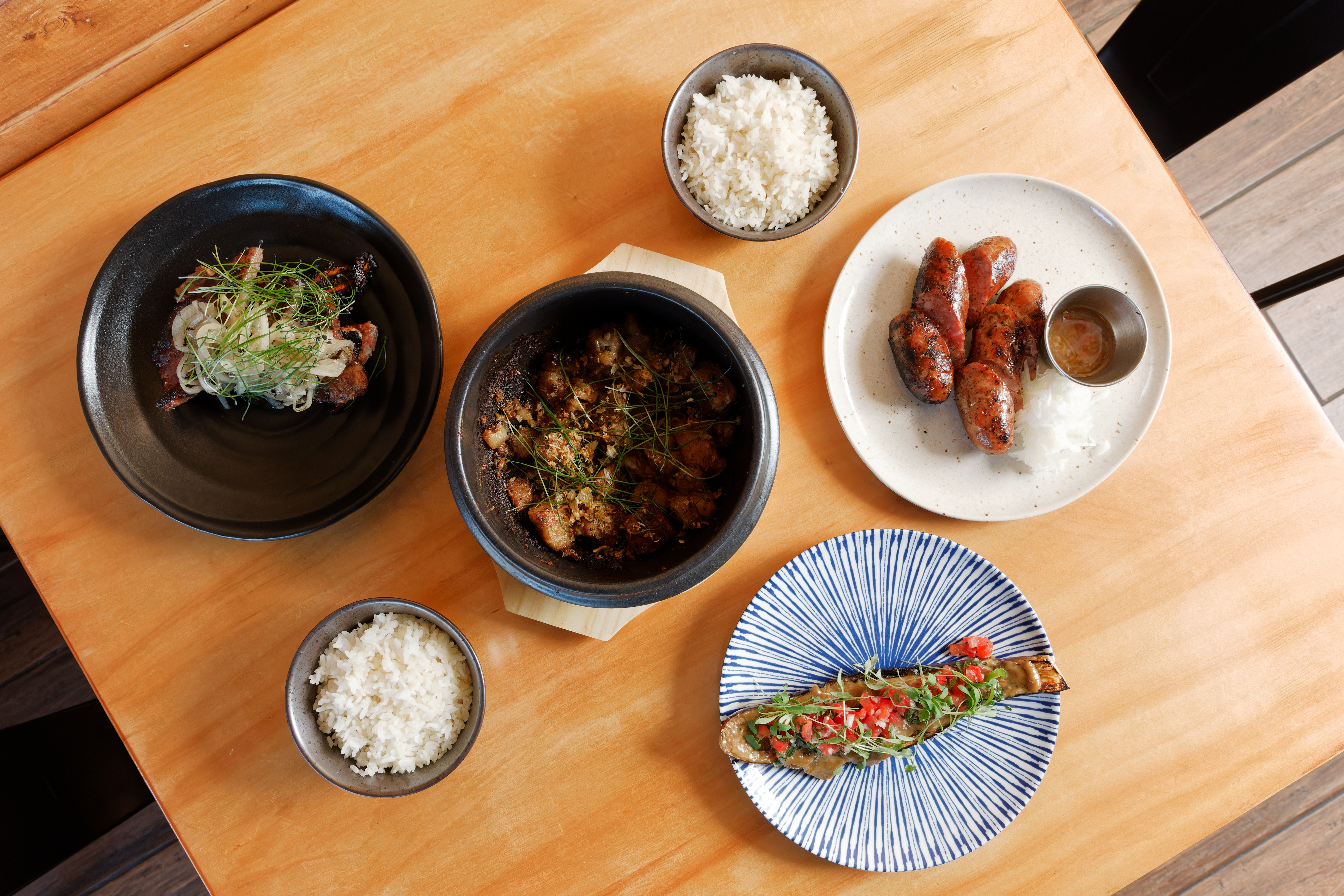 A wooden table laid with six dishes of various sizes, including bowls of rice and sliced sausage.