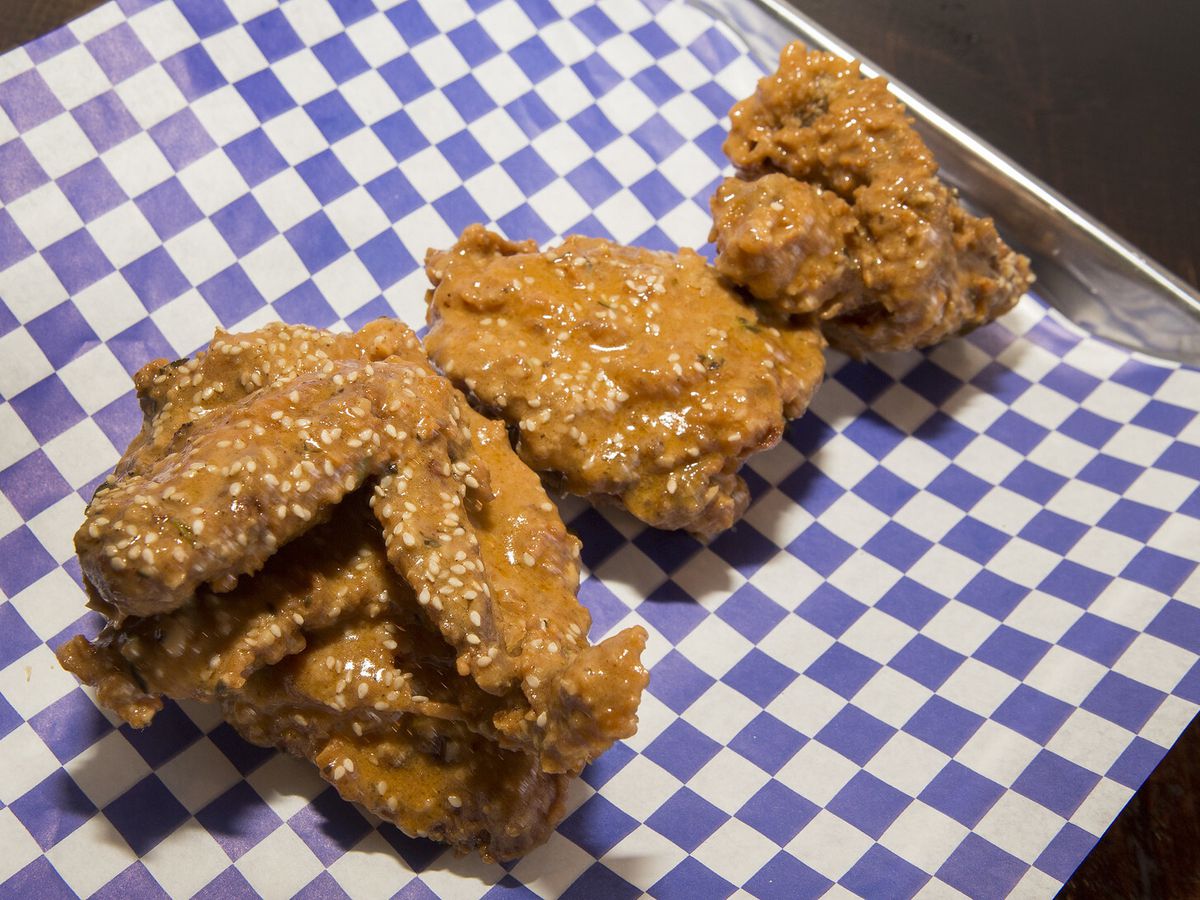 Pieces of fried chicken on blue and white checkered paper on a metal tray.