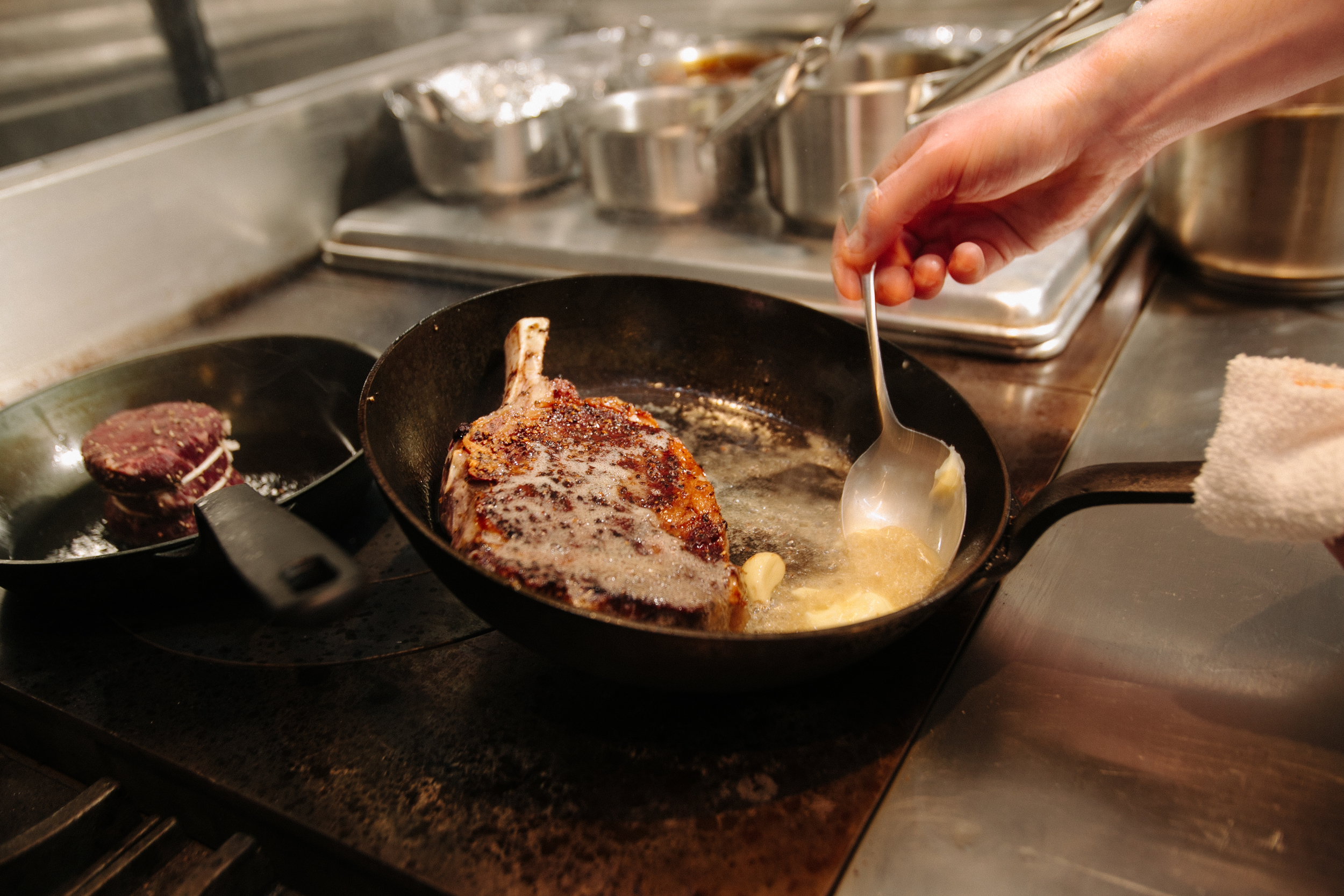 A chef bastes a steak in butter on a stove.