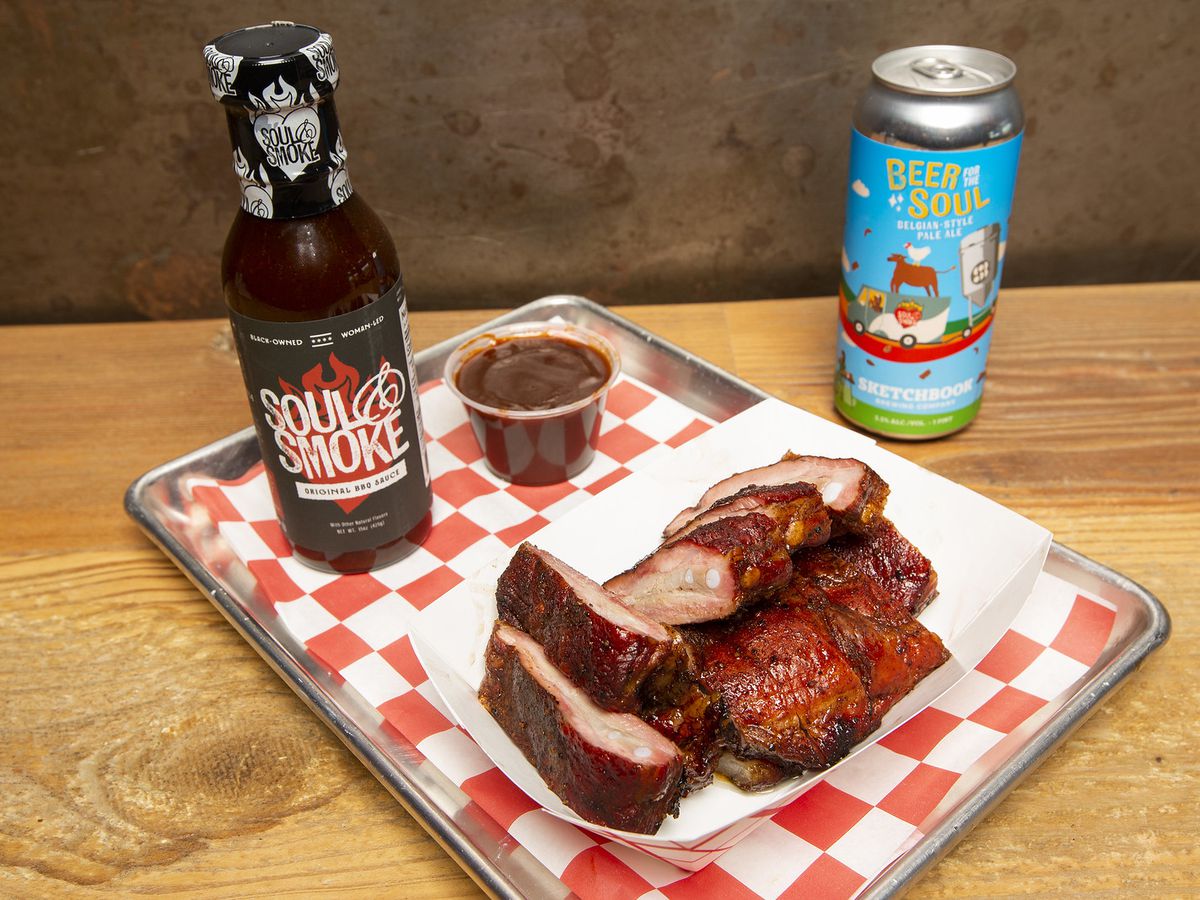 A platter of ribs, with a bottle of sauce and a can of beer.
