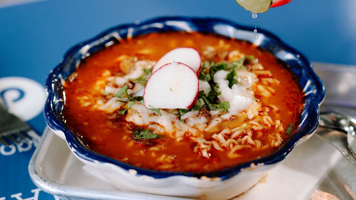 A hand squeezes lime juice onto a bowl of birria ramen.