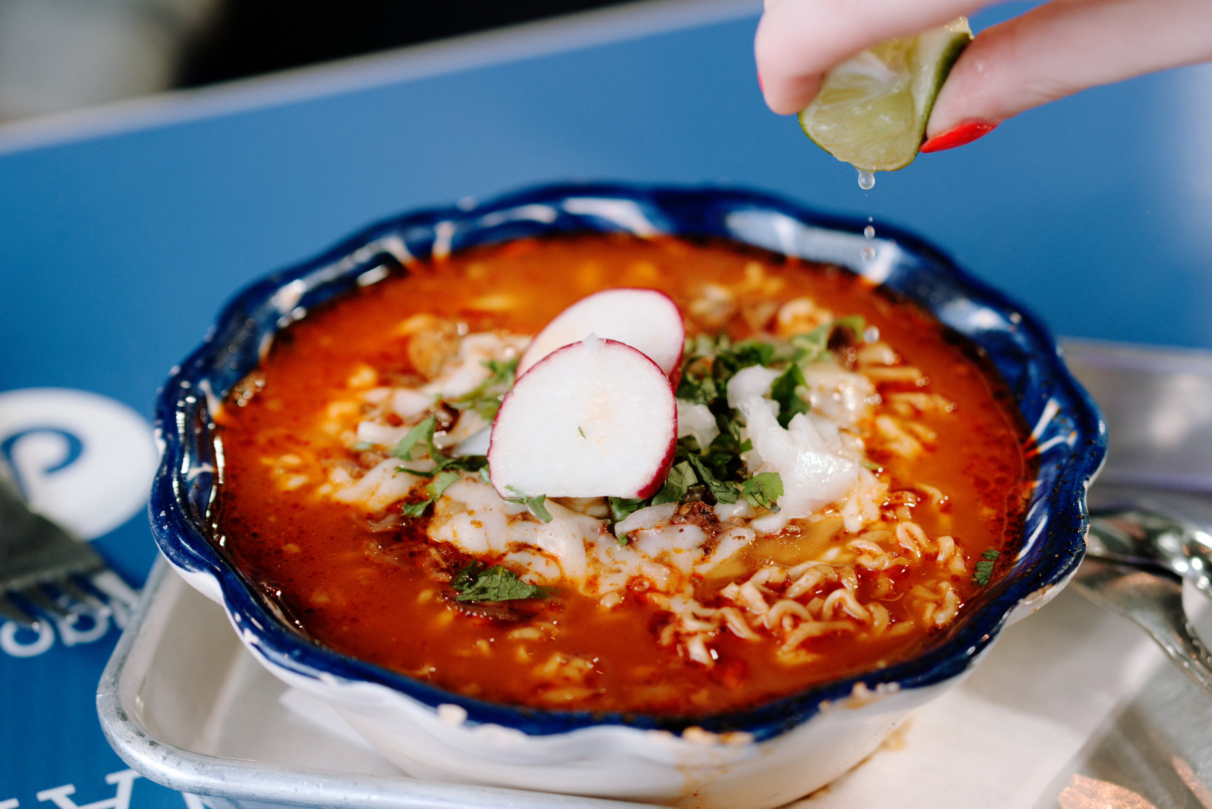 A hand squeezes lime juice onto a bowl of birria ramen.