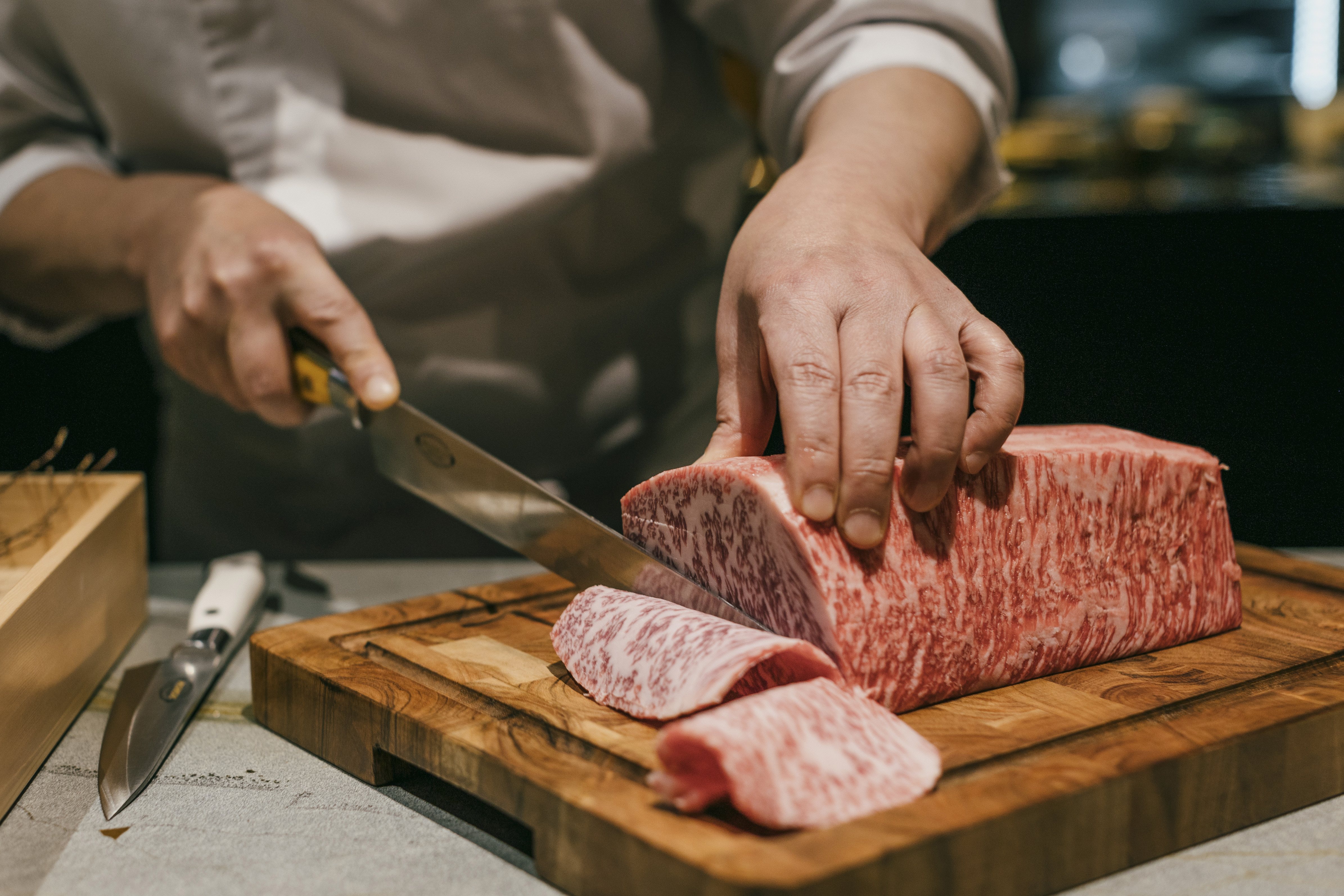 A chef slices a paper-thin piece of marbled beef with a large knife.