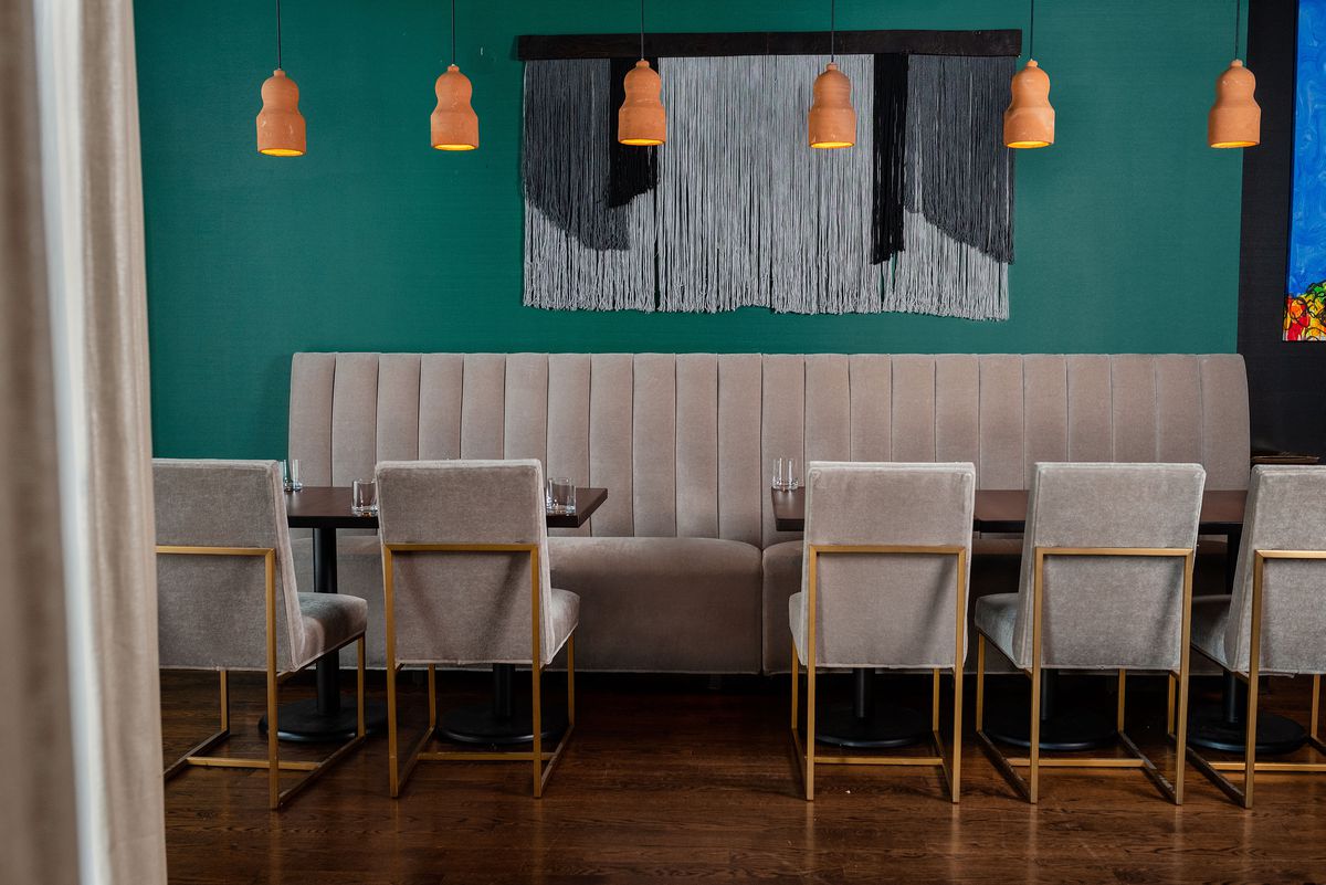 A long beige banquette along a turquoise wall. A row of hanging terracotta light fixtures is overhead.