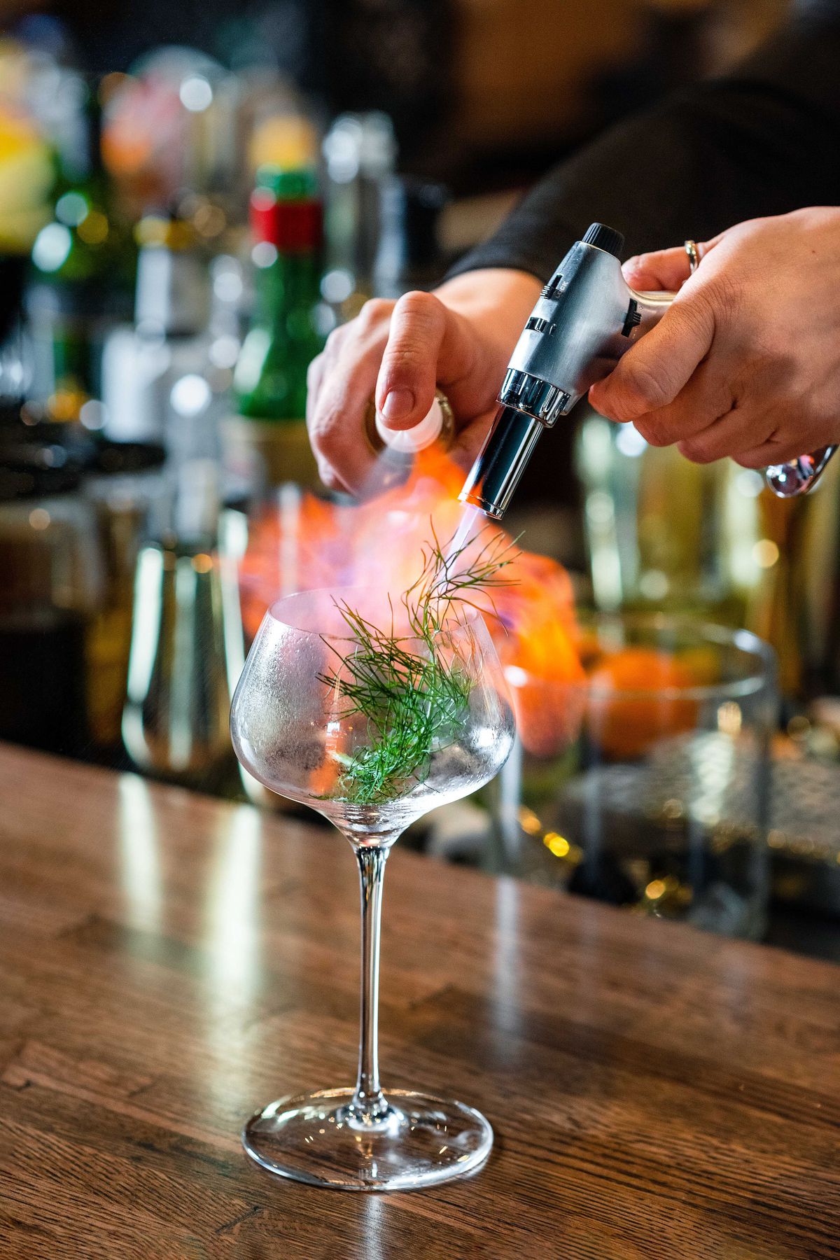 A bartender torches an anise front inside a cocktail glass while spraying it with Herbsaint.