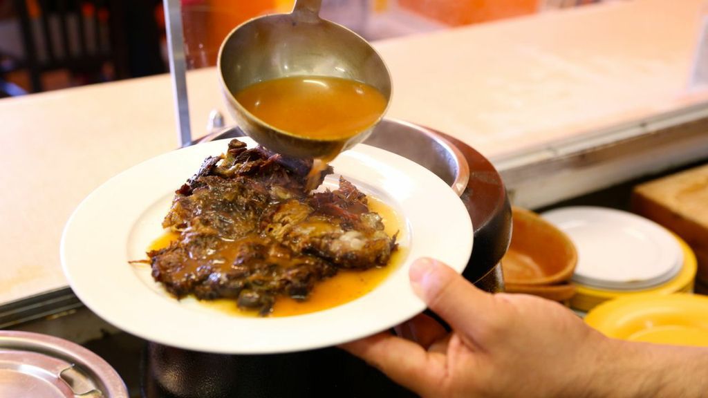A server ladles juices over a plate of goat meat.