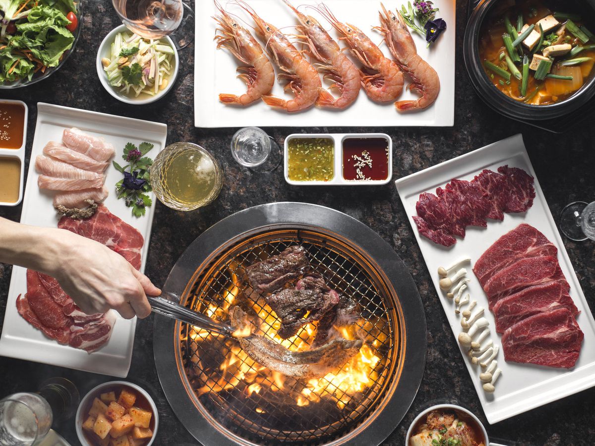 A person cooking meat on a grill that’s surrounded with more meats and side dishes.